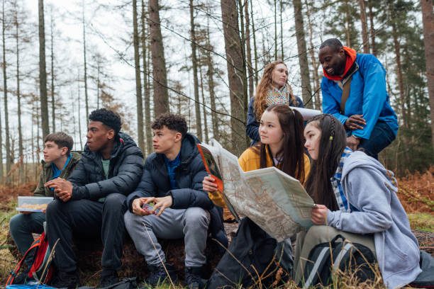 A medium shot of a group of teenage students and their two teachers on a field trip. They explore nature, blending lessons with the outdoors. They are reading from a map to guide their direction.

Video also available of this scenario